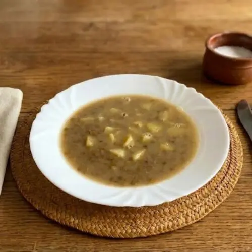 šošovicová polievka na kyslo v tanieri na stole s príborom a soľničkou